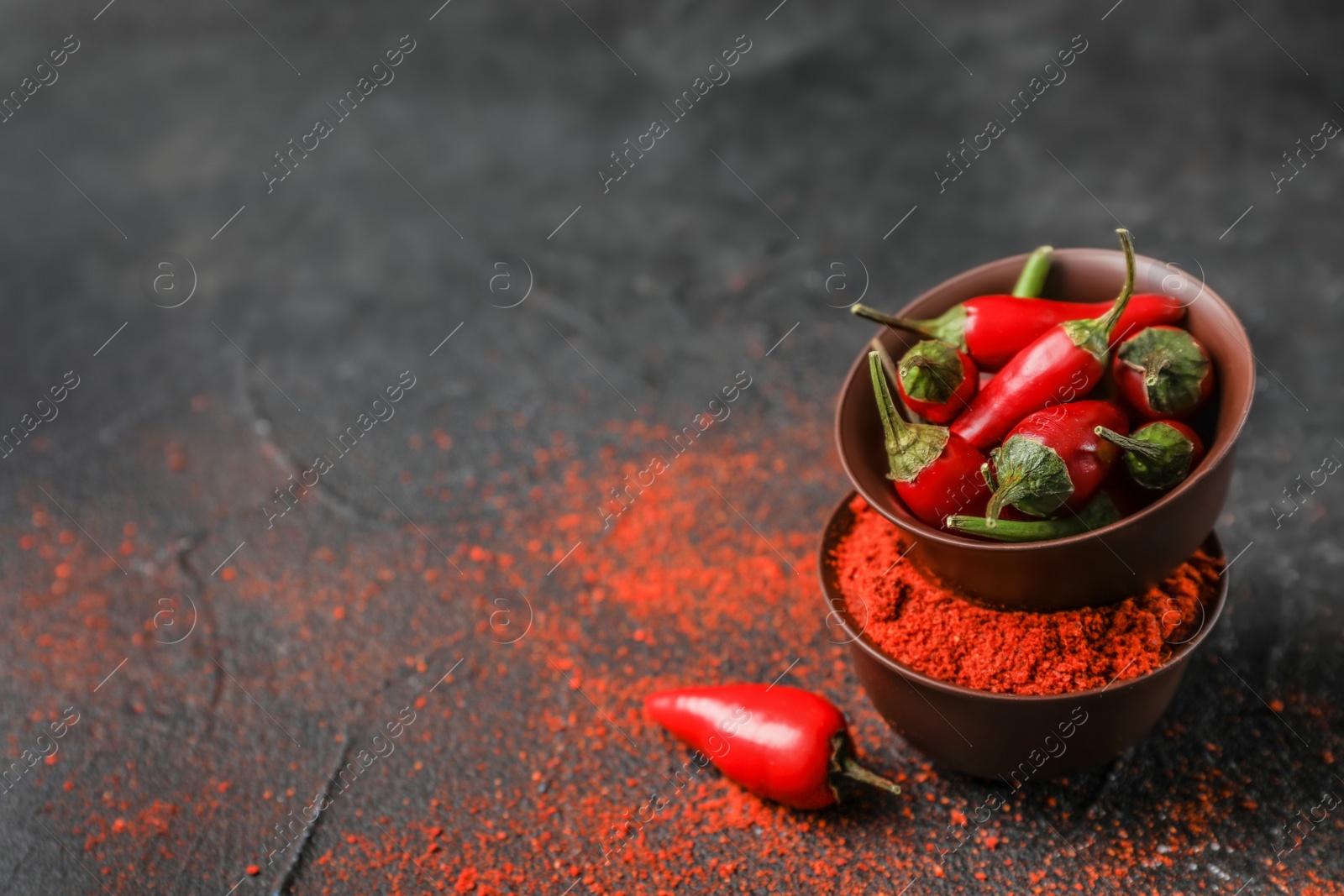 Photo of Bowls with raw and powdered chili peppers on dark table. Space for text