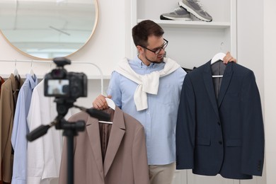 Photo of Fashion blogger showing clothes while recording video at home
