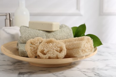 Photo of Loofah sponges, soap, towels and green leaves on white marble table