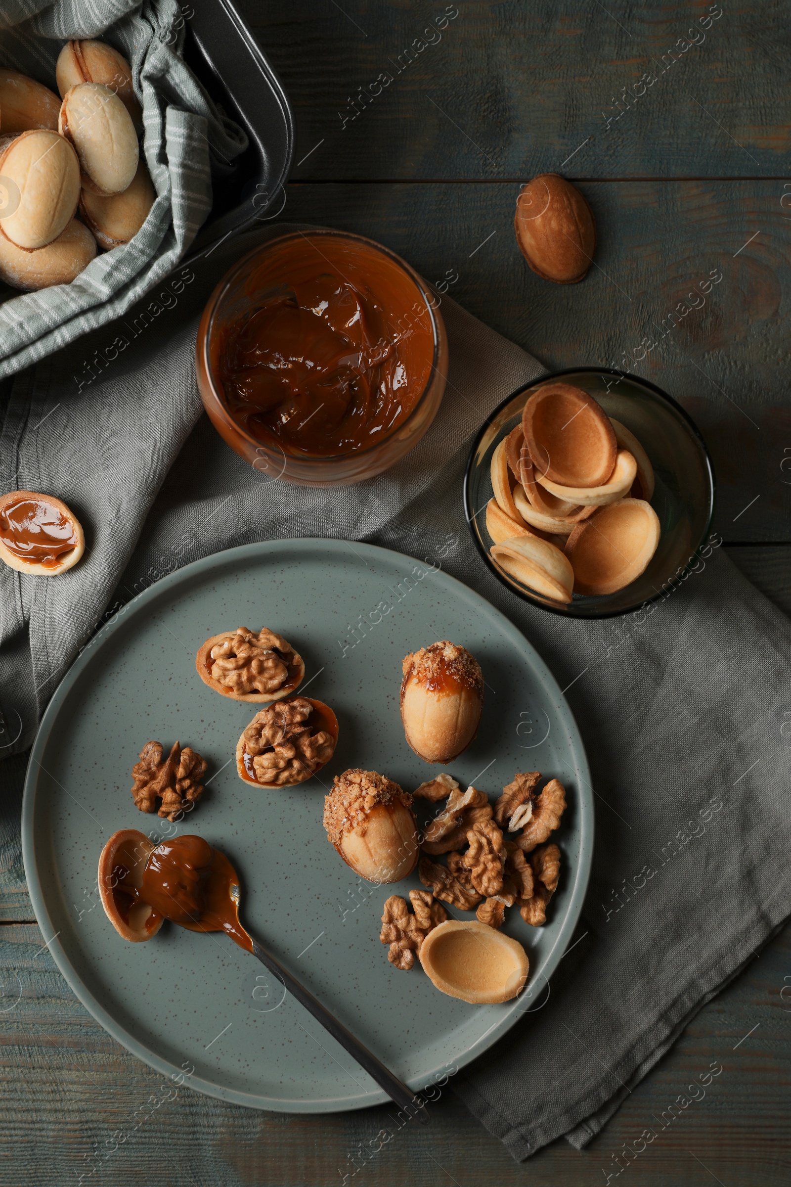 Photo of Freshly baked homemade walnut shaped cookies with nuts and boiled condensed milk on wooden table, flat lay