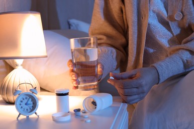 Photo of Woman taking pill in bedroom at night, closeup. Insomnia concept