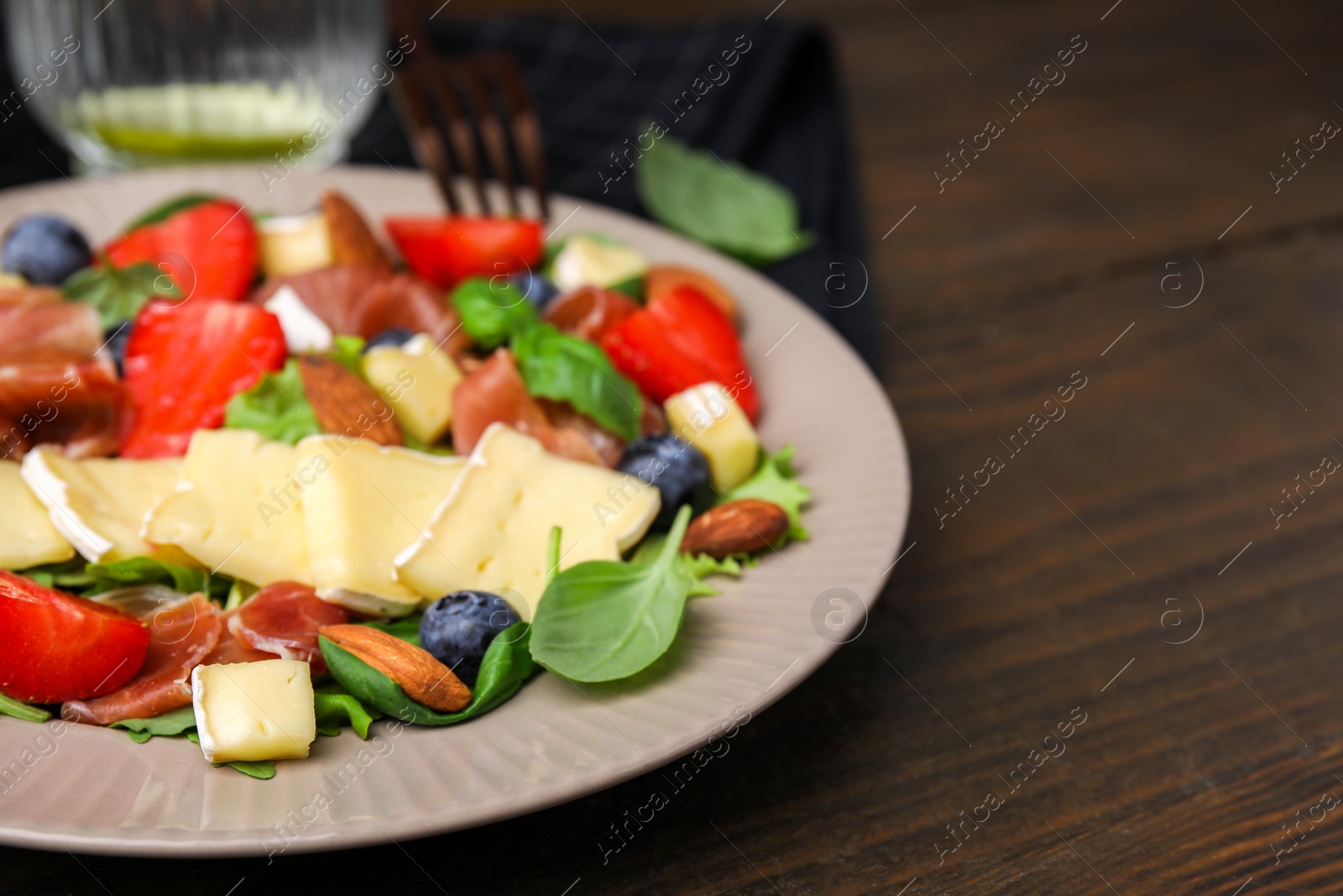 Photo of Tasty salad with brie cheese, prosciutto, almonds and berries on wooden table, closeup. Space for text