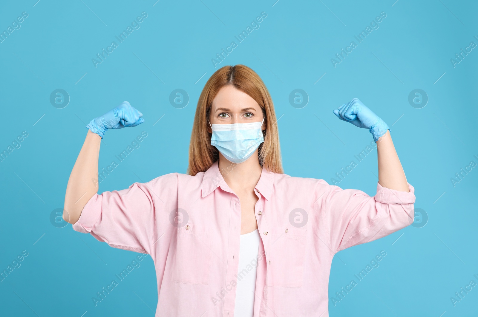 Photo of Woman with protective mask and gloves showing muscles on light blue background. Strong immunity concept