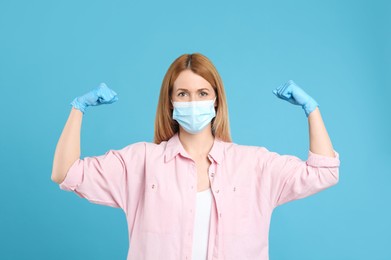 Photo of Woman with protective mask and gloves showing muscles on light blue background. Strong immunity concept