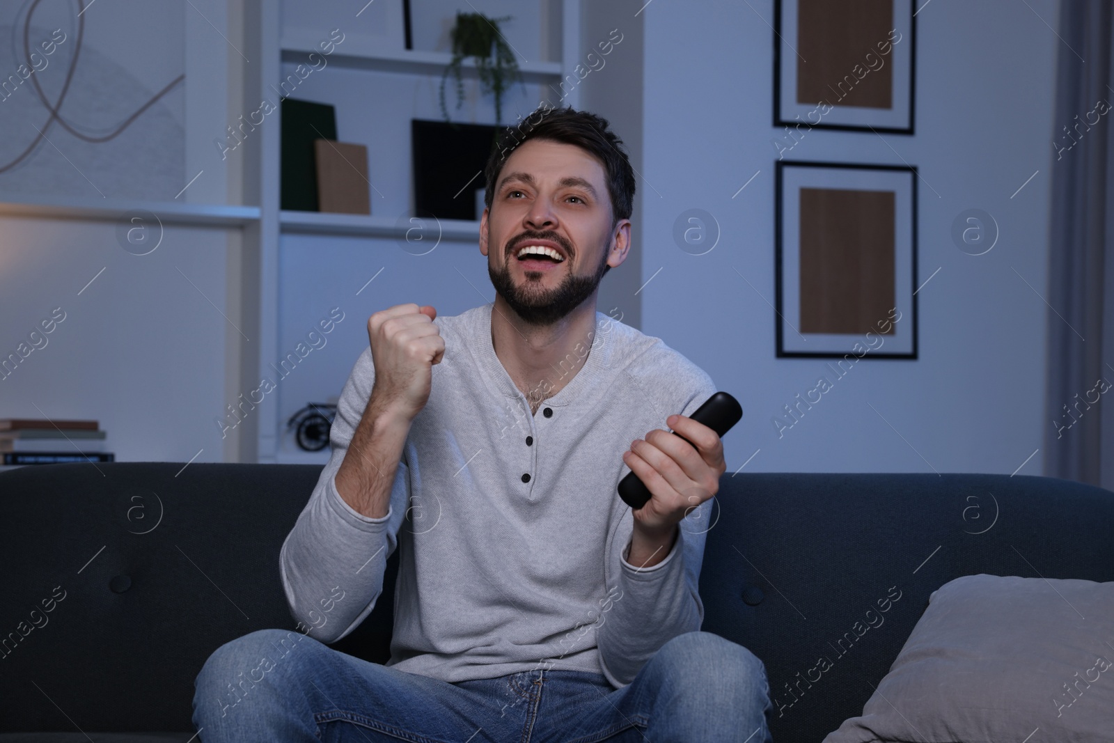 Photo of Emotional man with remote controller watching tv at home