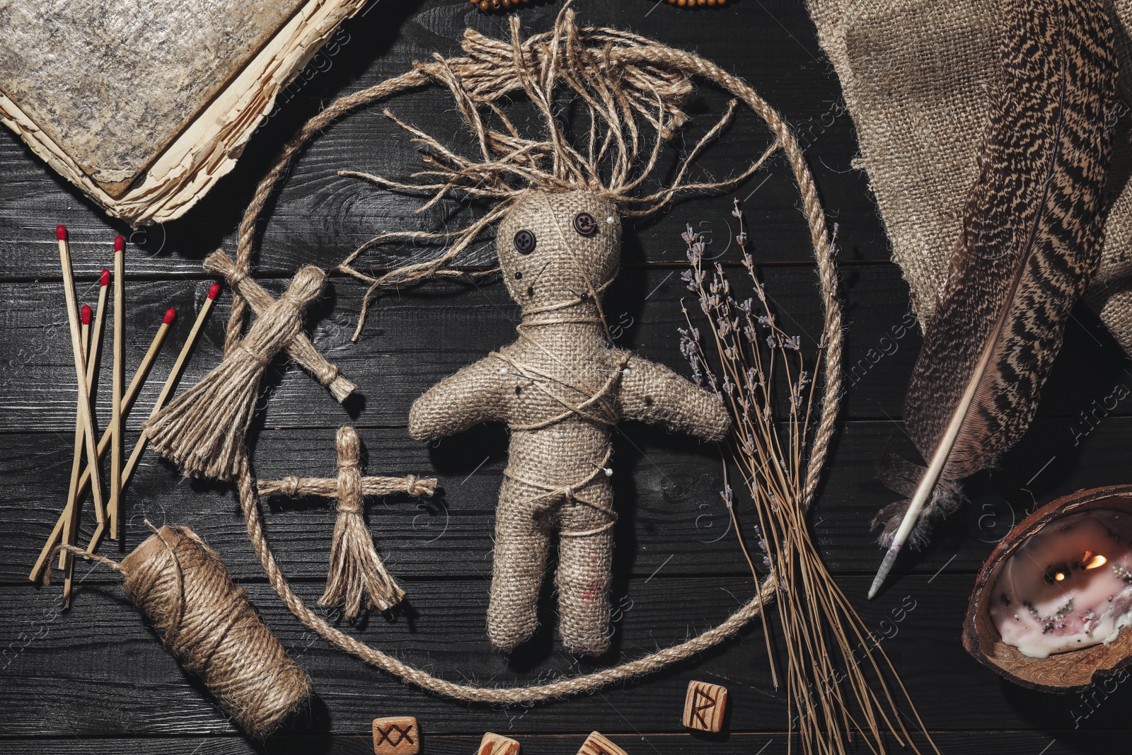 Photo of Female voodoo doll with pins surrounded by ceremonial items on black wooden background, flat lay