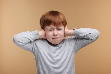 Photo of Hearing problem. Little boy suffering from ear pain on pale brown background