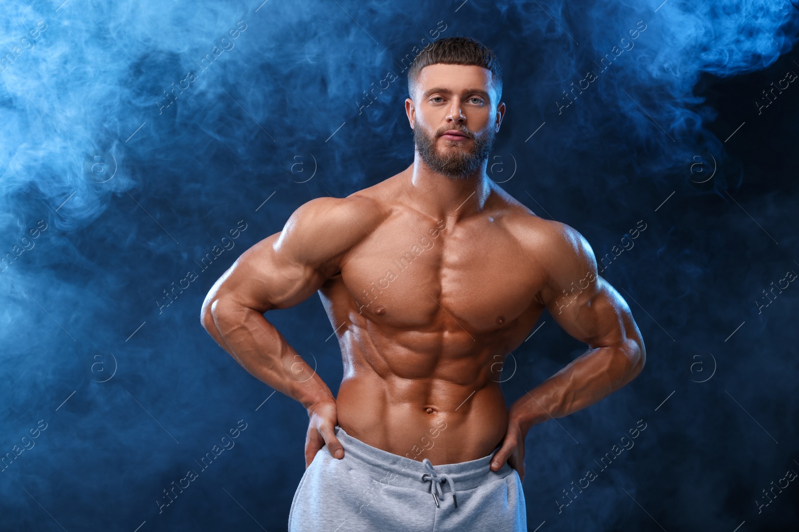 Photo of Young bodybuilder with muscular body in smoke on color background