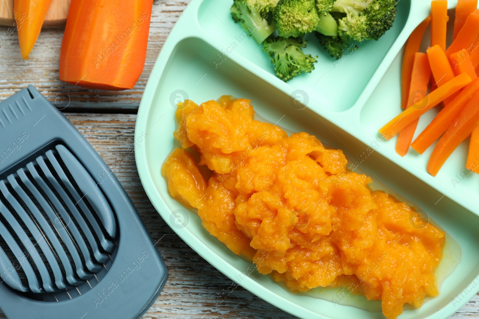 Photo of Baby food. Section plate with vegetables and pumpkin puree on rustic wooden table, flat lay