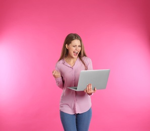 Emotional young woman with laptop celebrating victory on color background