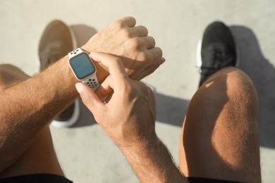 Man using modern smart watch during training outdoors, top view