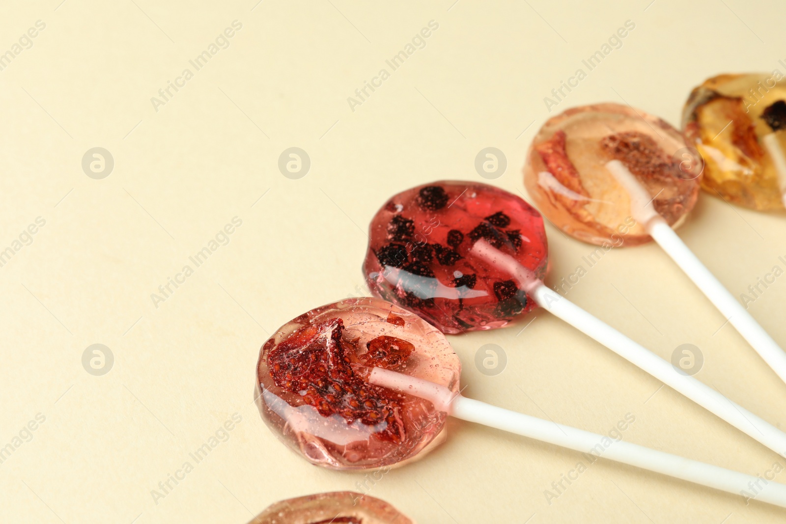 Photo of Sweet colorful lollipops with berries on beige background, closeup. Space for text