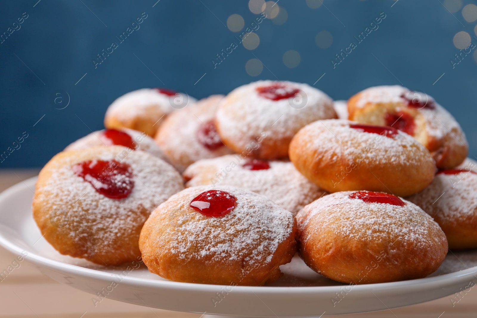 Photo of Hanukkah donuts with jelly and powdered sugar on stand against blurred festive lights, closeup