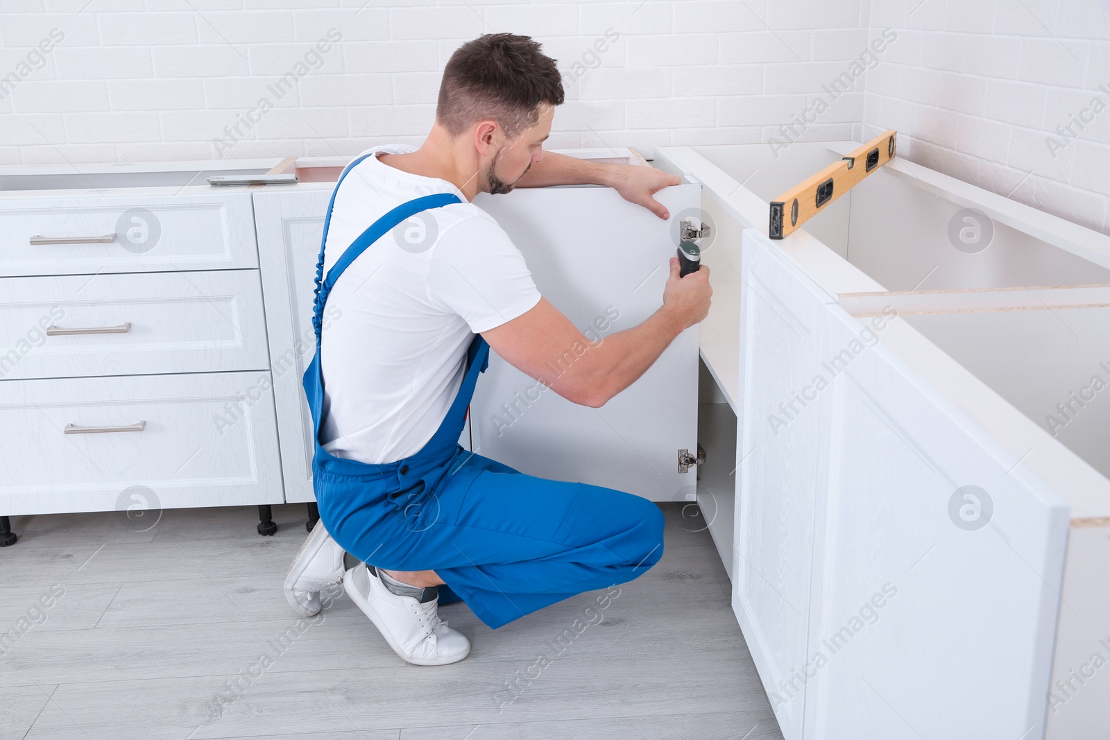 Photo of Worker installing door of cabinet in kitchen