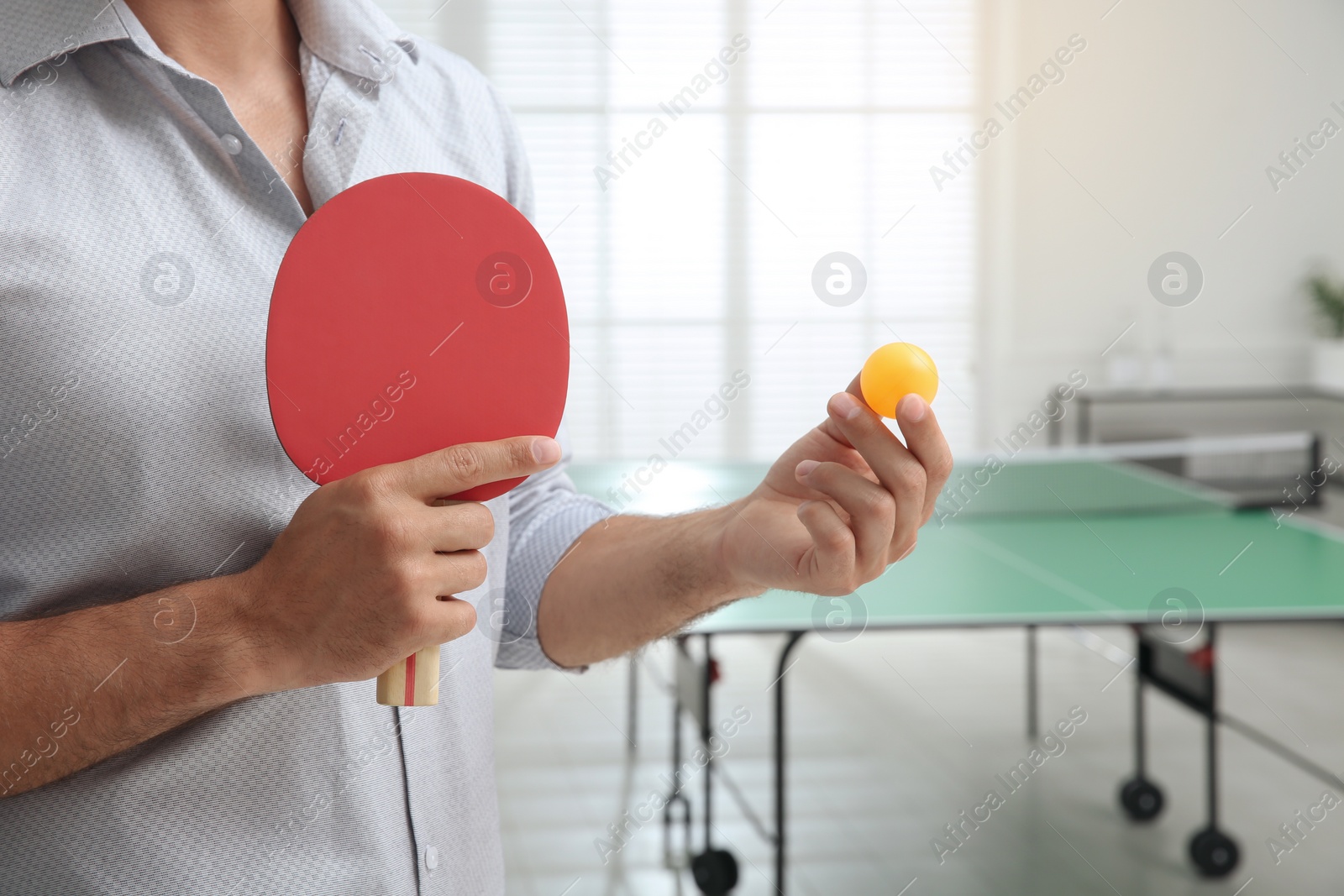 Photo of Businessman with tennis racket and ball near ping pong table in office, closeup