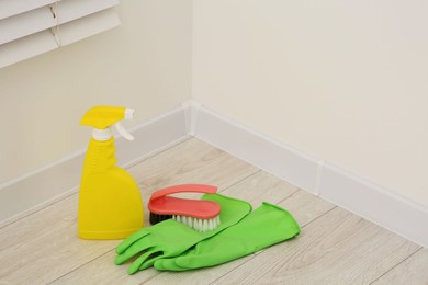 Photo of Spray bottle of cleaning product, rubber gloves and brush indoors