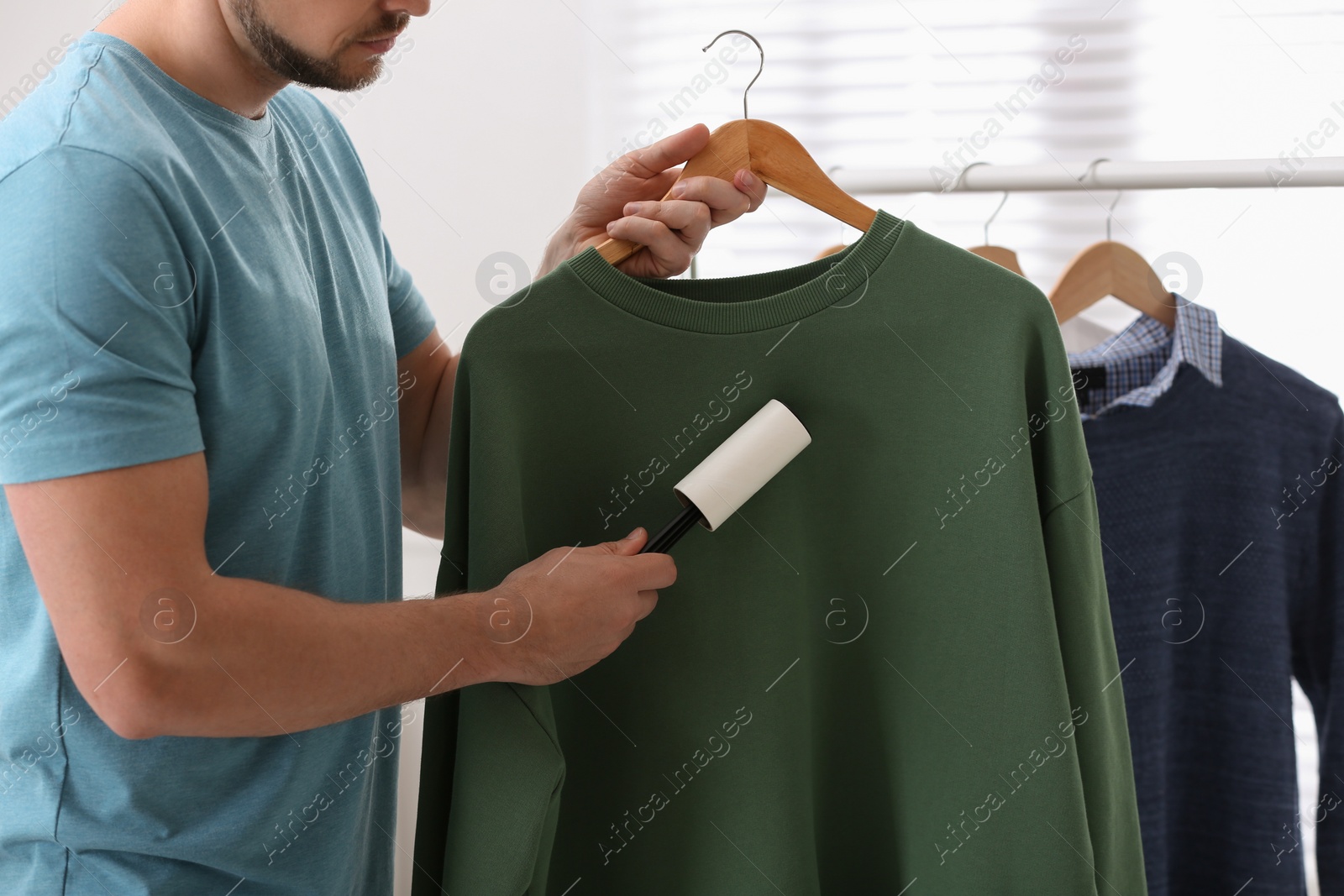 Photo of Man cleaning clothes with lint roller indoors, closeup