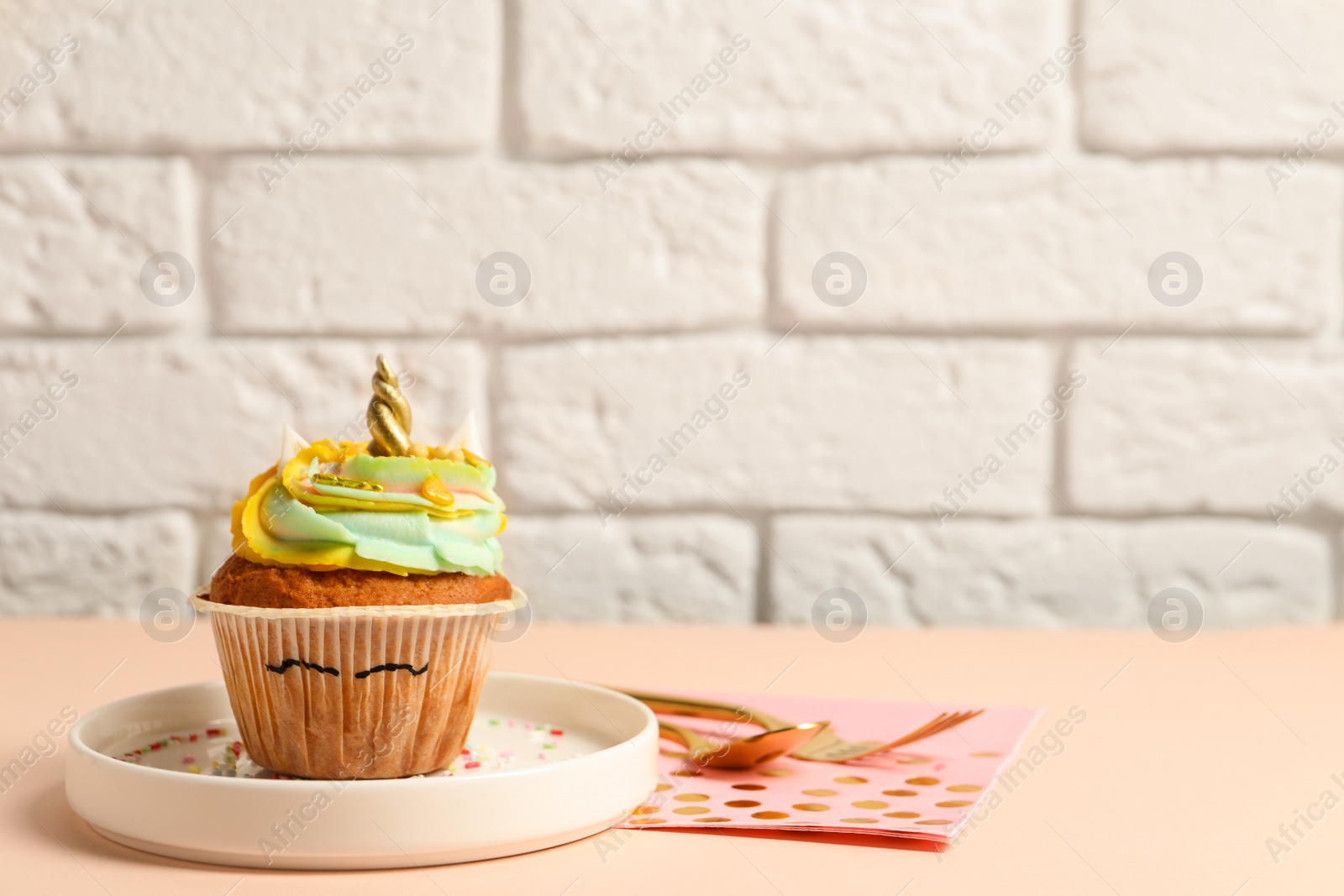 Photo of Plate with cute sweet unicorn cupcake on beige table, space for text