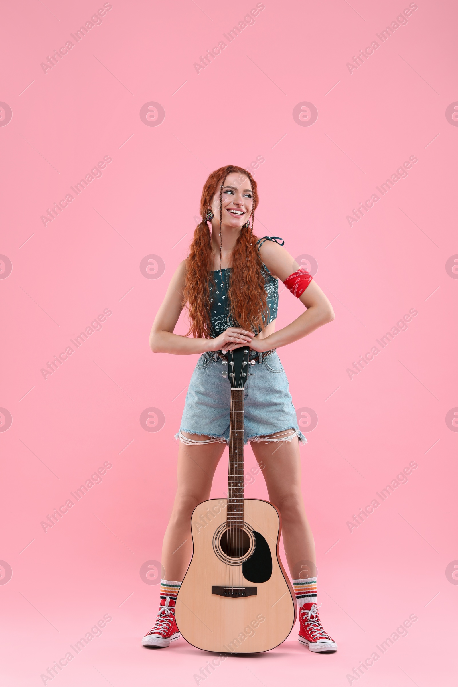 Photo of Stylish young hippie woman with guitar on pink background