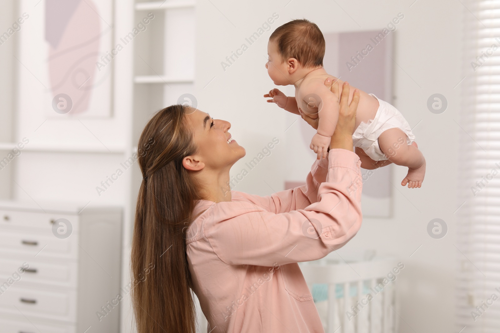 Photo of Mother having fun her cute newborn baby in child's room