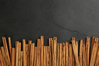 Aromatic cinnamon sticks on black table, flat lay. Space for text