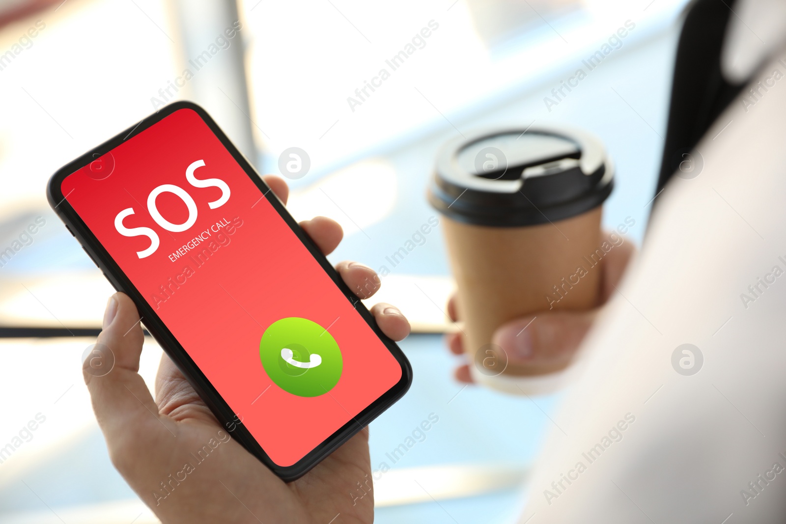 Image of Man holding smartphone with emergency call SOS on screen indoors, closeup