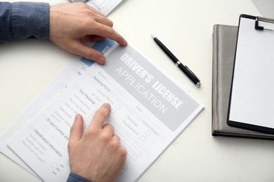 Man with driver's license application form at white table, above view