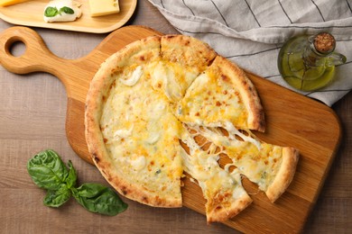 Delicious cut cheese pizza and ingredients on wooden table, flat lay