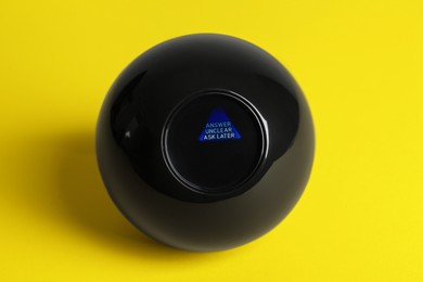 Photo of Magic eight ball with prediction Answer Unclear Ask Later on yellow background