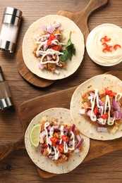 Delicious tacos with vegetables, meat and sauce on wooden table, flat lay