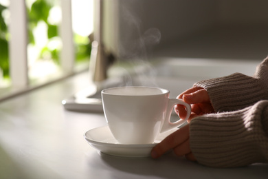 Photo of Woman with cup of tasty coffee at home, closeup. Good morning