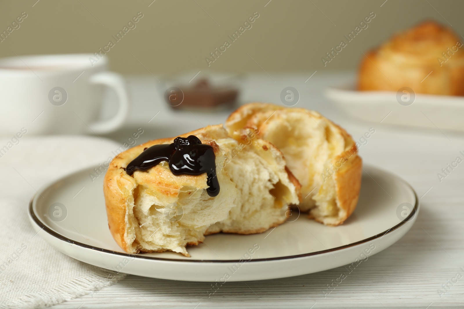Photo of Delicious bun with chocolate sauce on white wooden table