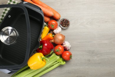 Photo of Black pot, lid and fresh products on wooden table, top view. Space for text