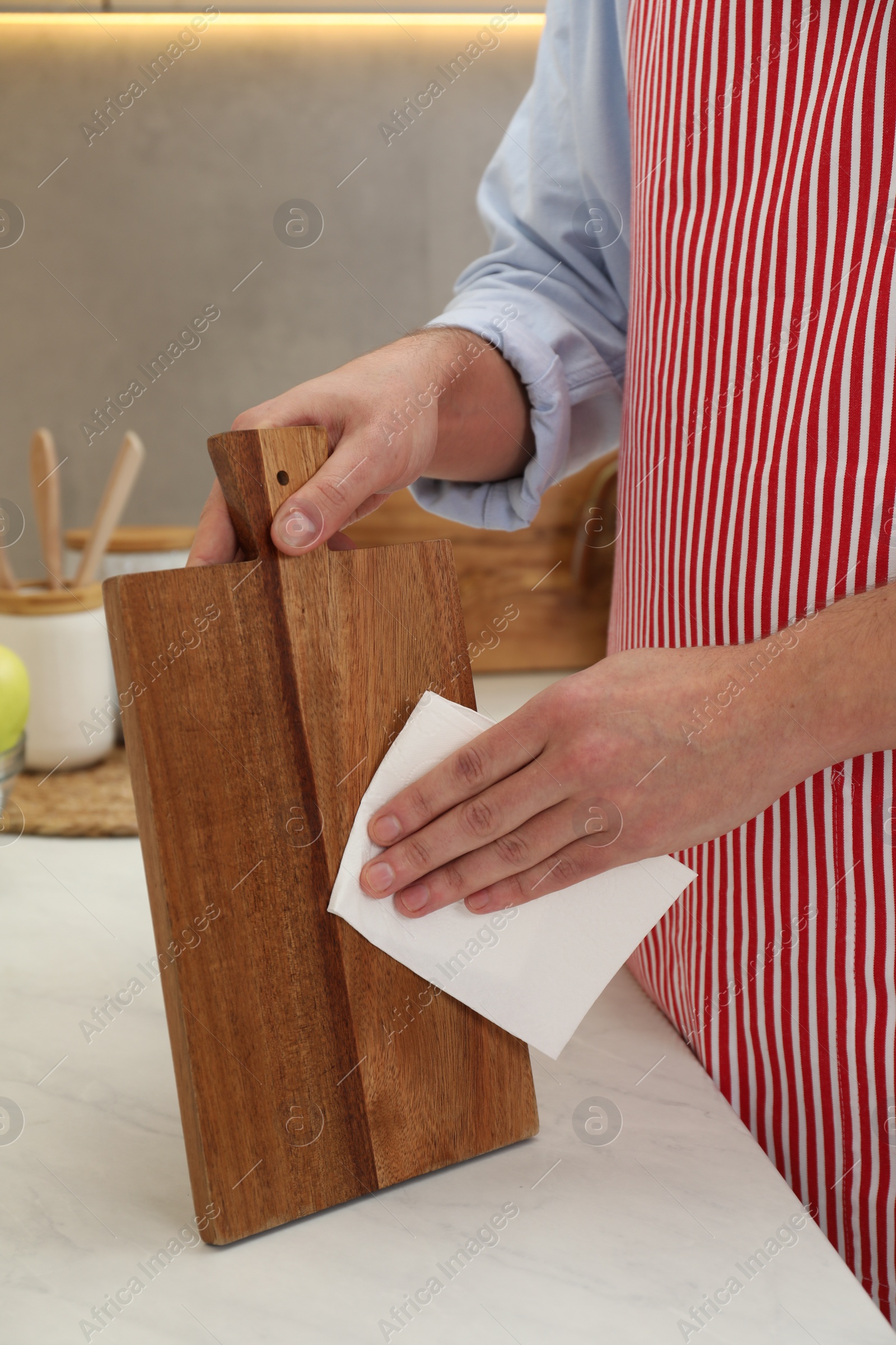 Photo of Man wiping wooden cutting board with paper napkin at white table, closeup