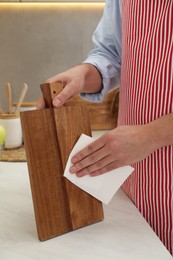 Photo of Man wiping wooden cutting board with paper napkin at white table, closeup