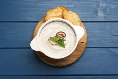 Photo of Fresh homemade mushroom soup in ceramic pot on blue wooden table, top view