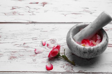 Photo of Mortar with pestle and rose petals on white wooden table, space for text