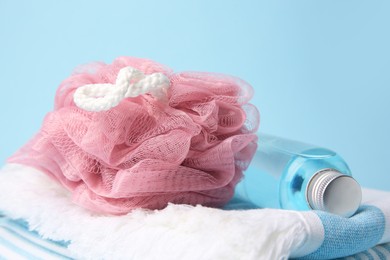 Photo of Pink shower puff, bottle of cosmetic product and towel on light blue background, closeup