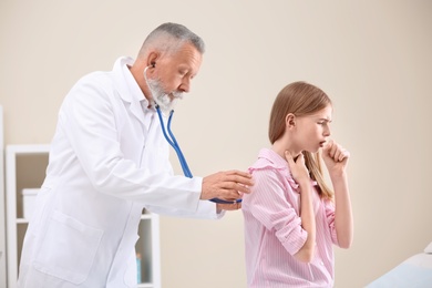 Doctor examining coughing teenage girl at clinic