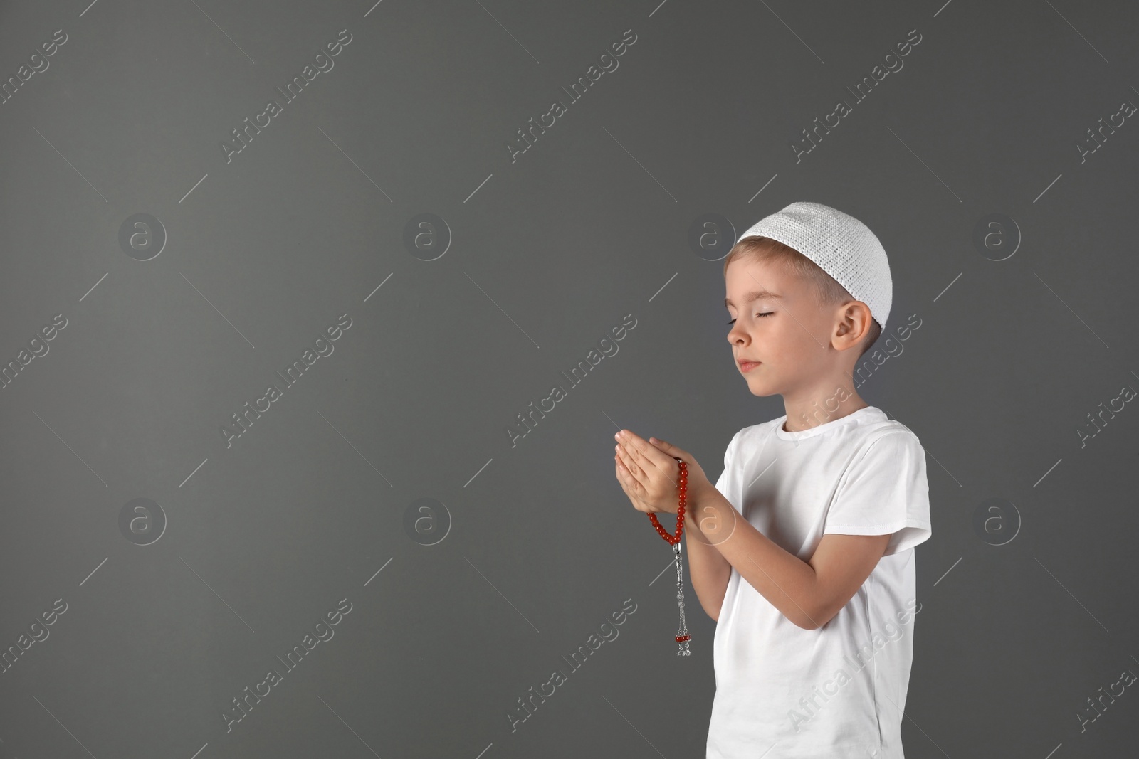 Photo of Little Muslim boy praying on gray background. Space for text