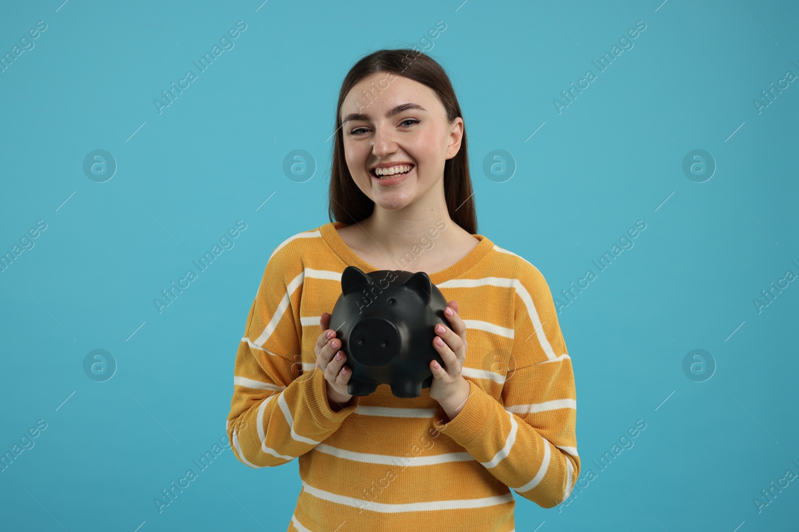 Photo of Happy woman with piggy bank on light blue background