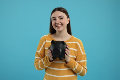 Happy woman with piggy bank on light blue background