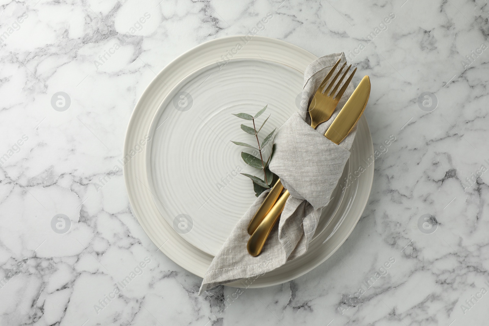 Photo of Stylish setting with cutlery, napkin, eucalyptus branch and plates on white marble table, top view