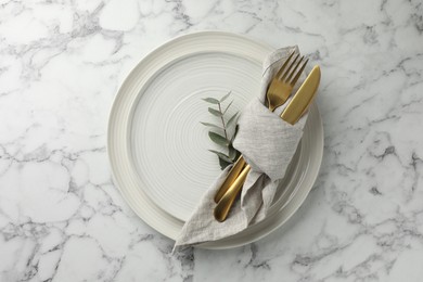 Stylish setting with cutlery, napkin, eucalyptus branch and plates on white marble table, top view