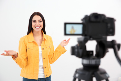 Photo of Young blogger recording video on camera against white background
