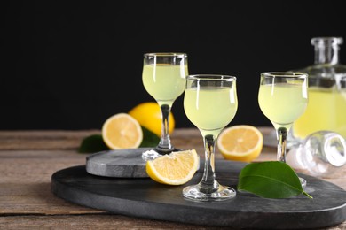 Photo of Tasty limoncello liqueur, lemons and green leaves on wooden table. Space for text
