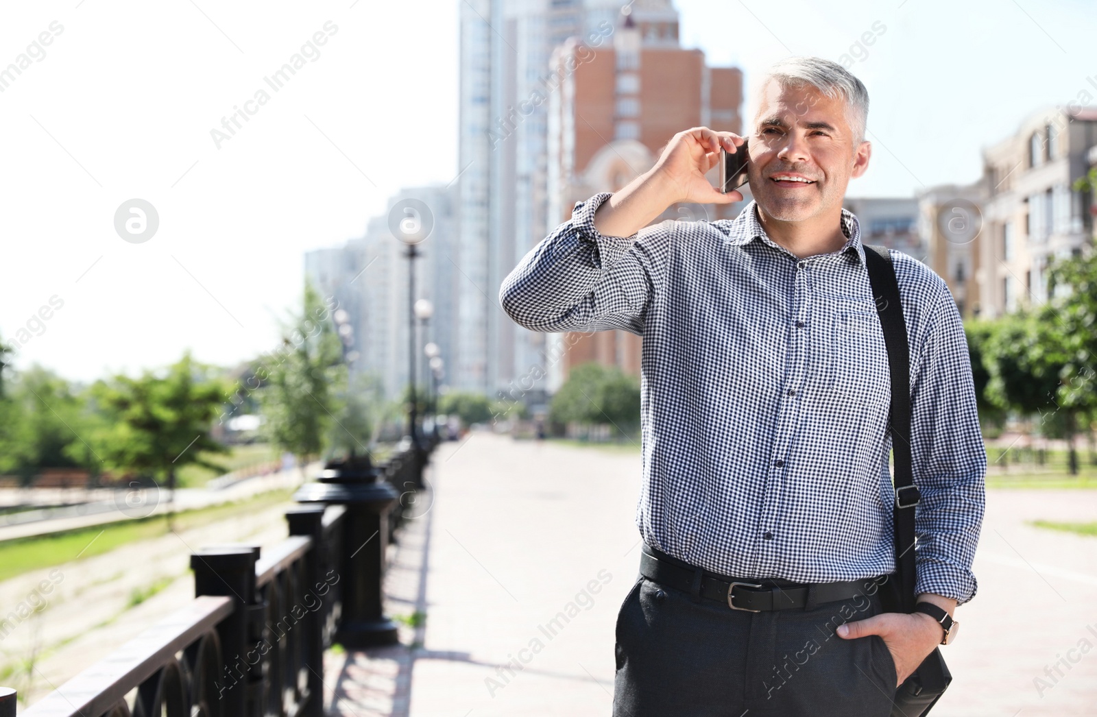 Photo of Handsome businessman talking by mobile phone in city, space for text