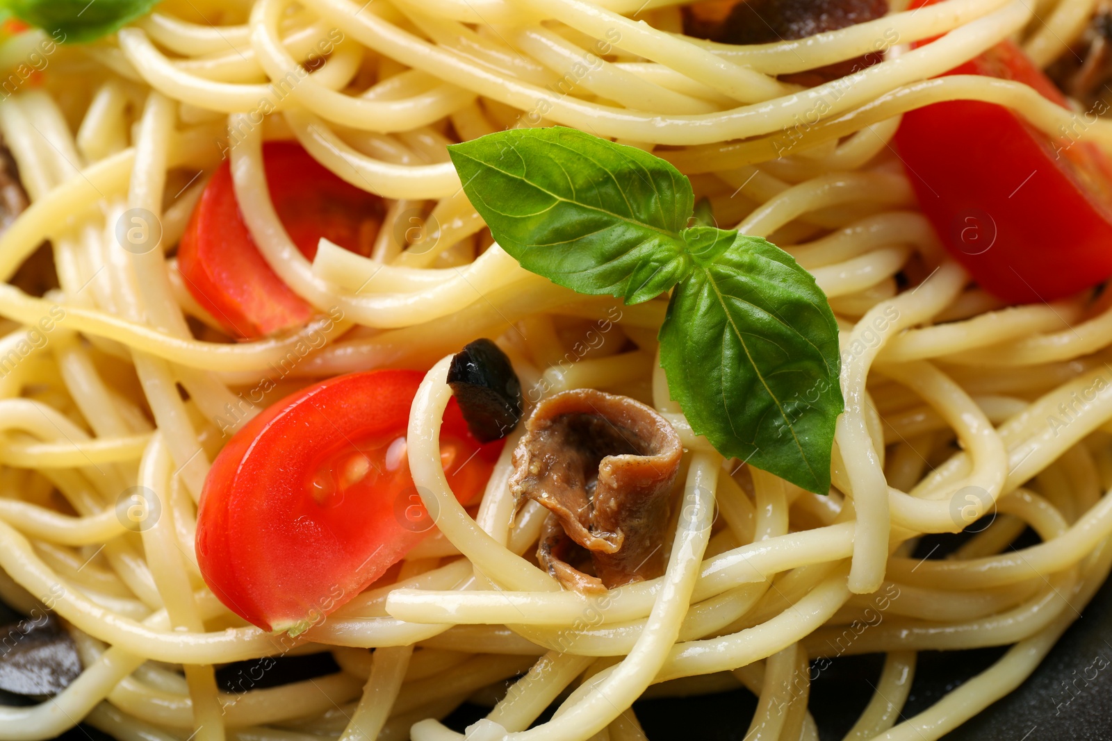 Photo of Delicious pasta with anchovies, tomatoes and basil as background, closeup