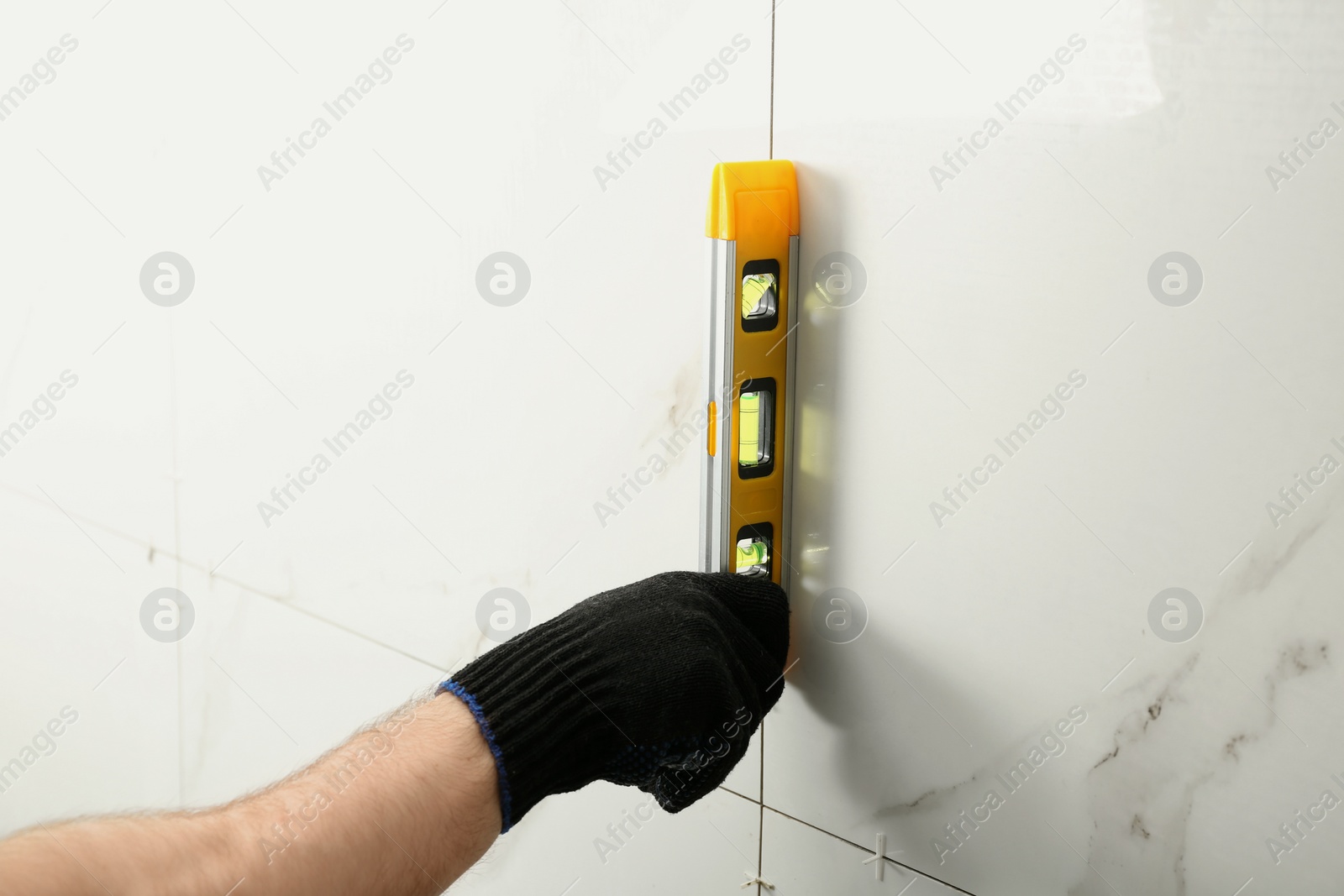 Photo of Man checking proper ceramic tile installation with level on wall, closeup. Building and renovation works