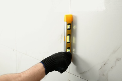 Photo of Man checking proper ceramic tile installation with level on wall, closeup. Building and renovation works